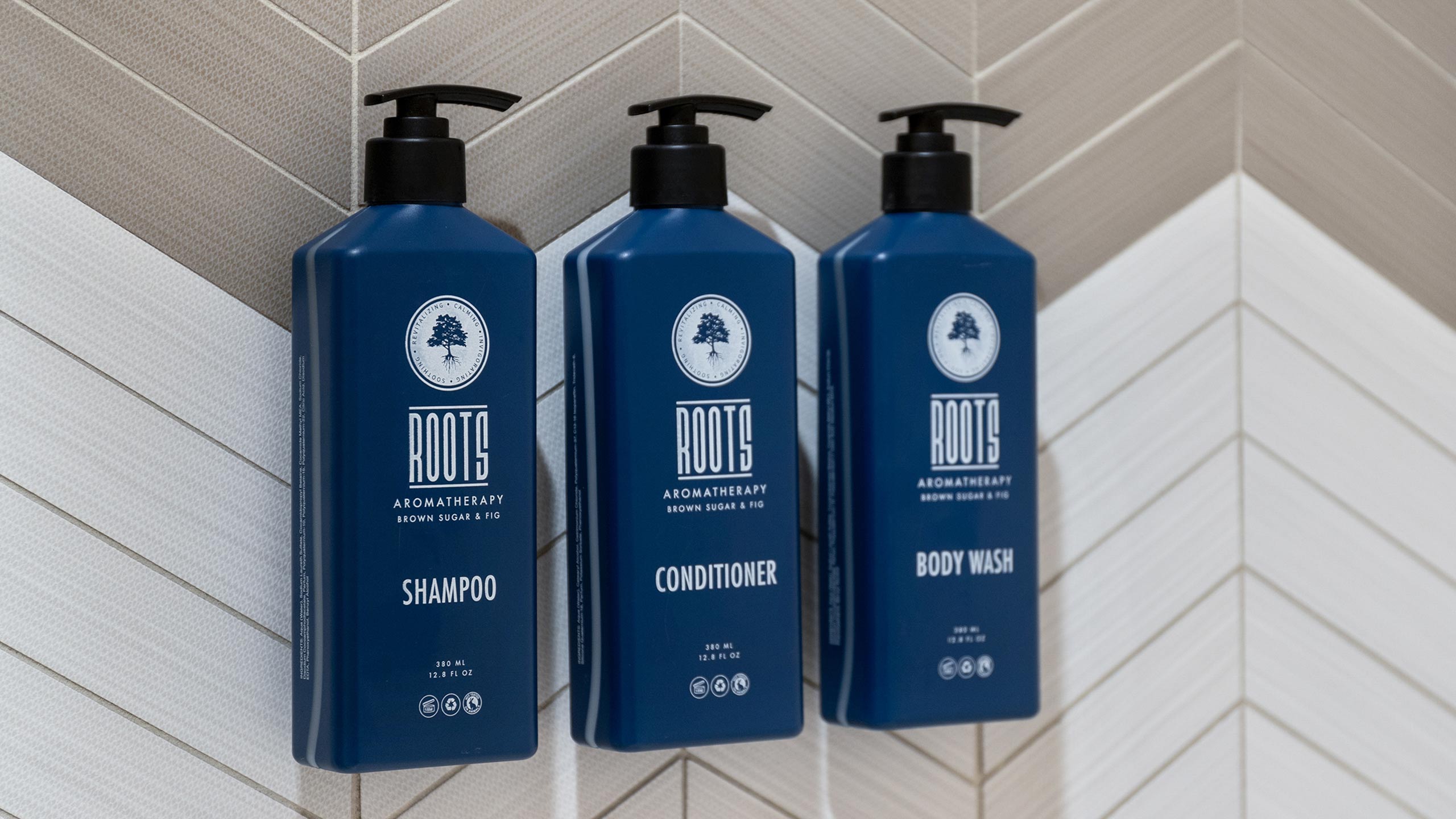 Three blue Roots bulk toiletry bottles hanging on a chevron tile wall in the bathroom of a club resort