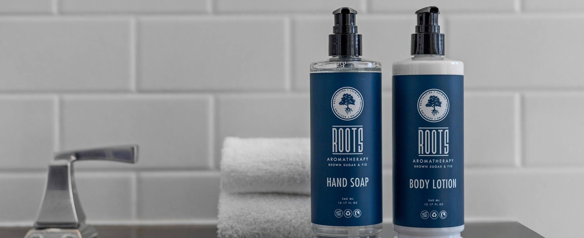 Two blue Roots bulk amenity bottles on the bathroom counter of a club resort with a set of towels folded behind them