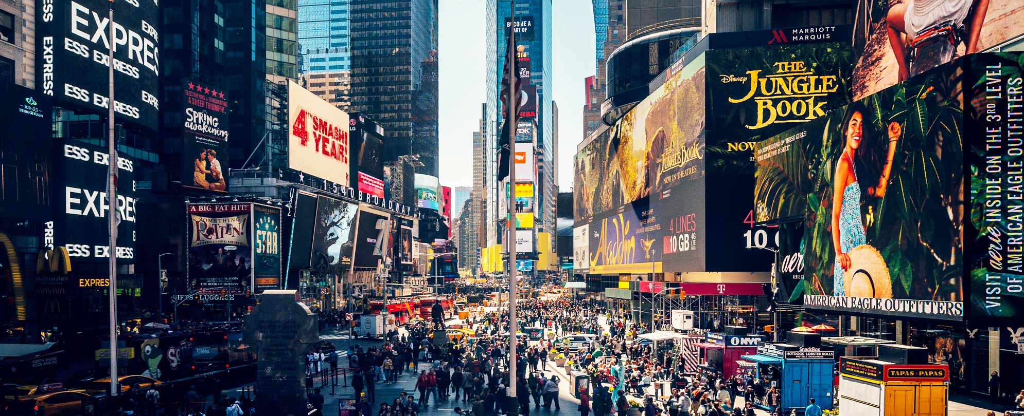 A crowded street in Times Square with large billboards advertising movies and Broadway musicals