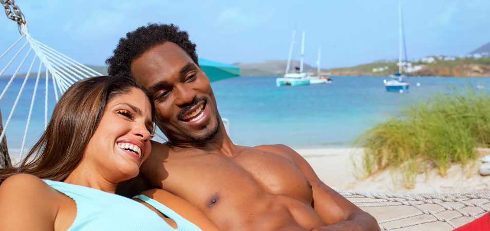 Man and woman smiling, laying in a hammock by the ocean at a Margaritaville Vacation Club timeshare resort.