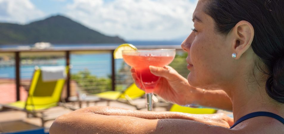 A woman looking at the view of the ocean as she enjoys a Margarita in hand.  