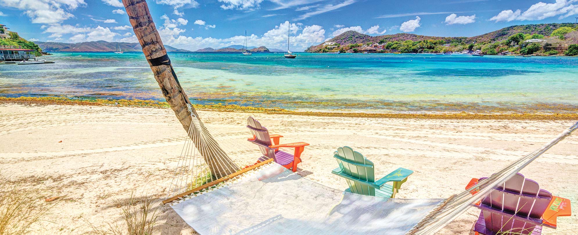  A hammock between palm trees and three Adirondack chairs on a beach by Margaritaville Vacation Club — St. Thomas.