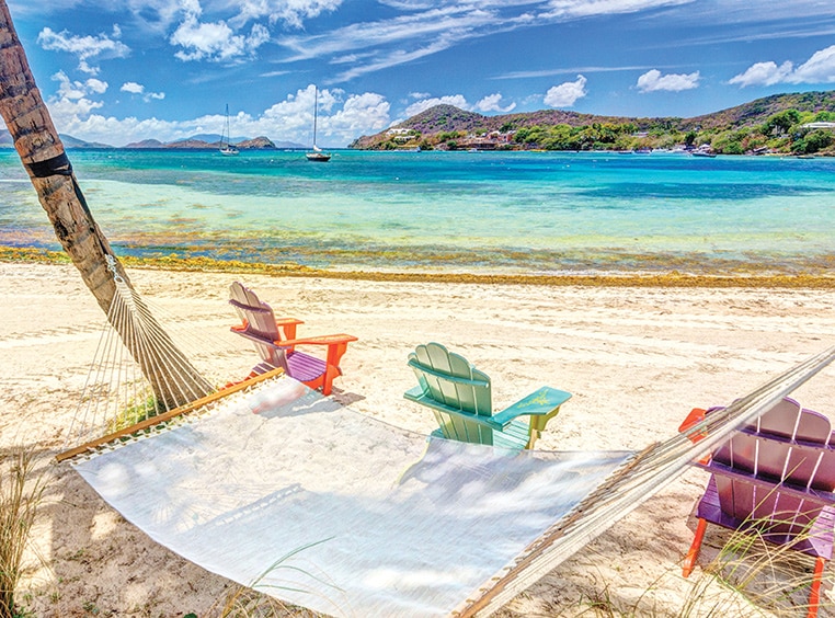  A hammock between palm trees and three Adirondack chairs on a beach by Margaritaville Vacation Club — St. Thomas.