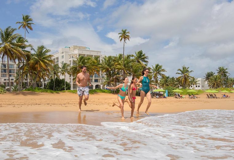 Mom, dad, and two young daughters running into the ocean on vacation at Margaritaville Vacation Club by Wyndham - Rio Mar.