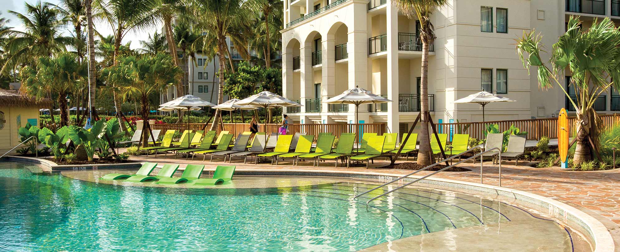 Bright green pool chairs and palm trees surround the shimmering pool at a Margaritaville Vacation Club resort.