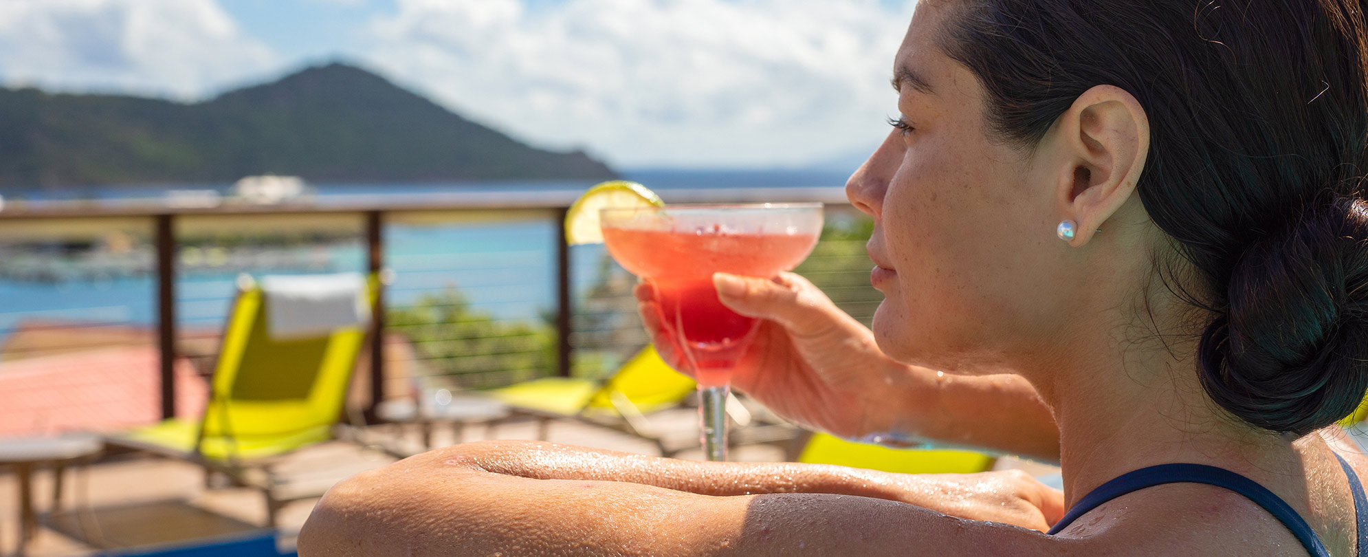 Dark-haired woman looks out over the ocean with a pink margarita in hand, relaxing at a Margaritaville Vacation Club resort.