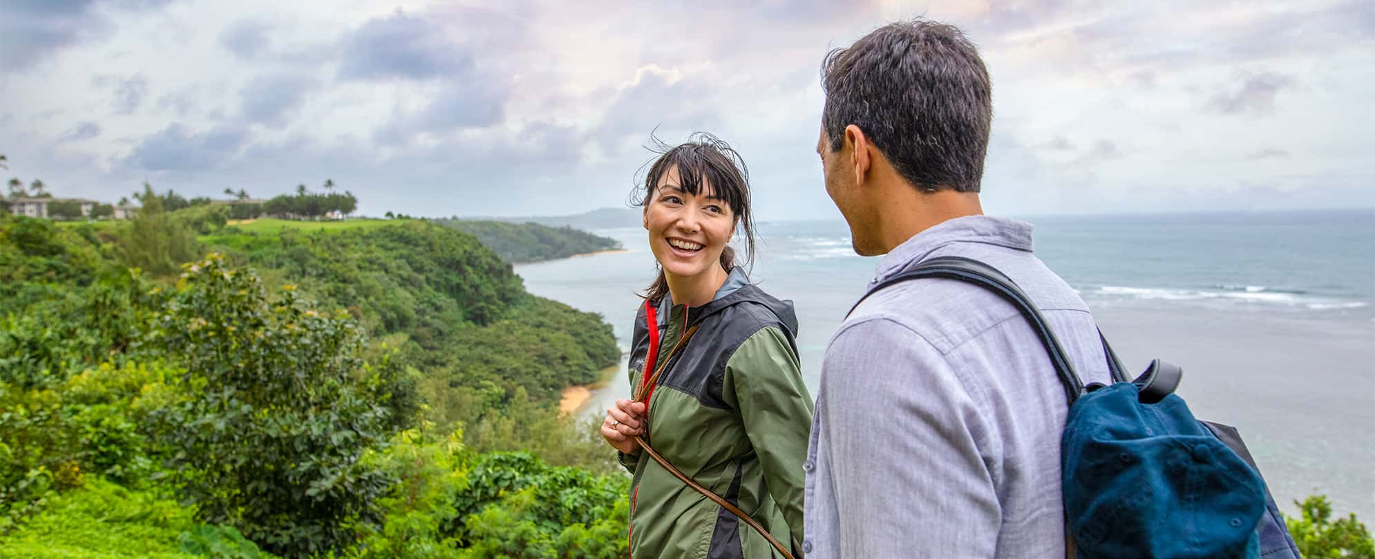 A couple on vacation hiking through lush mountains overlooking the ocean. 