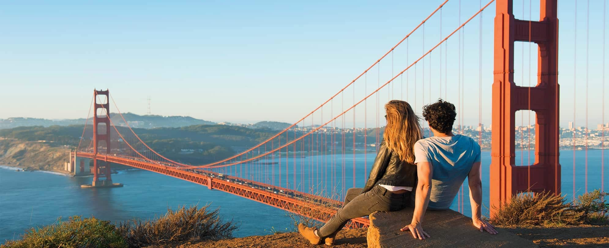 A couple sitting close together looking at an incredible view of the Golden Gate Bridge in San Francisco, CA. 