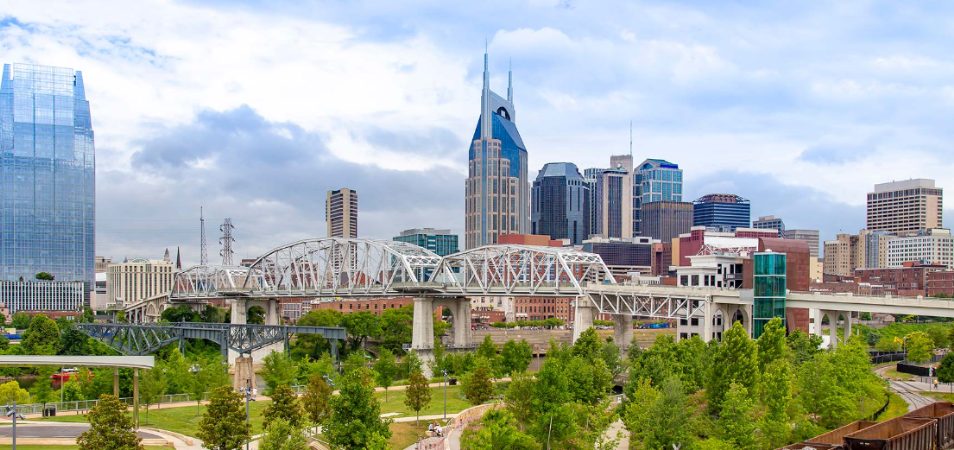 The pedestrian bridge and city skyline of Nashville, Tennessee on a clear, sunny day.