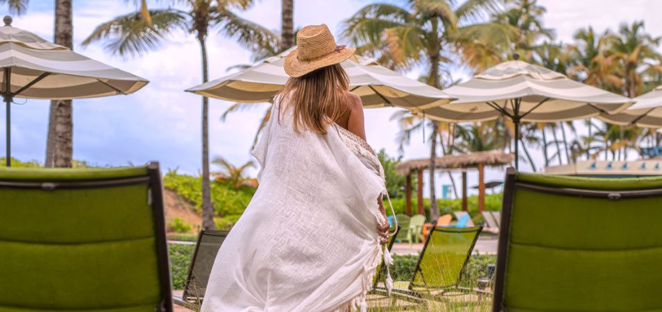 Blonde woman in hat and white flowing cover up walking towards the pool at a Margaritaville Vacation Club resort.