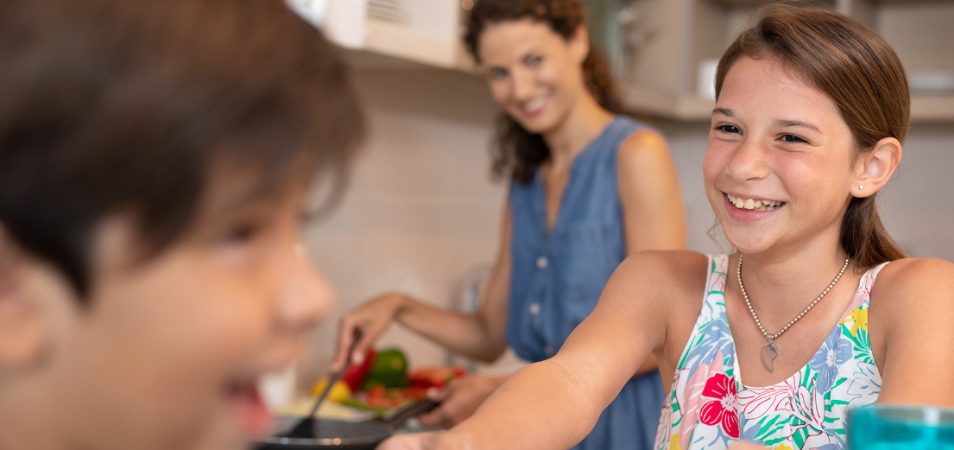 Mom cooks a meal for two smiling kids in the kitchen of their Margaritaville Vacation Club resort suite.