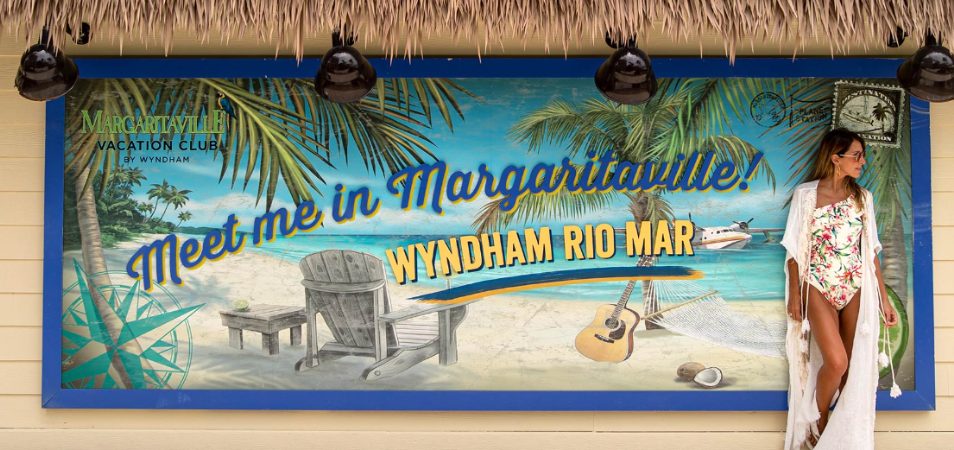 Woman standing by of sign that reads "Meet Me in Margaritaville. Wyndham Rio Mar" at a Margaritaville Vacation Club resort.