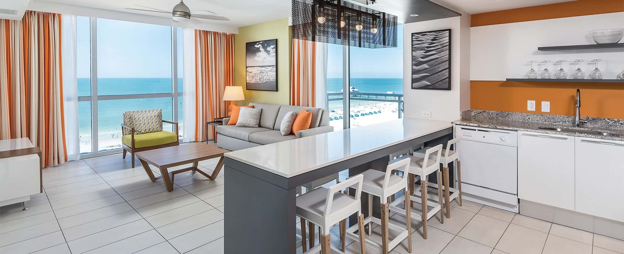 A modern living room and kitchen in a Margaritaville Vacation Club suite with a view of the ocean.