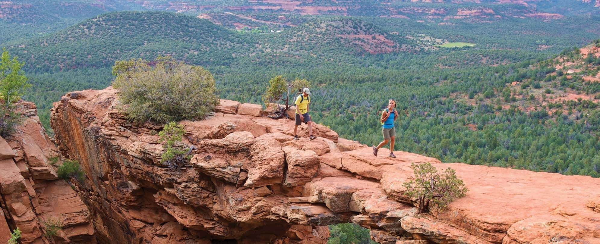 Couple wearing backpacks hiking on a red rock formation during their Margaritaville Vacation Club adventures.