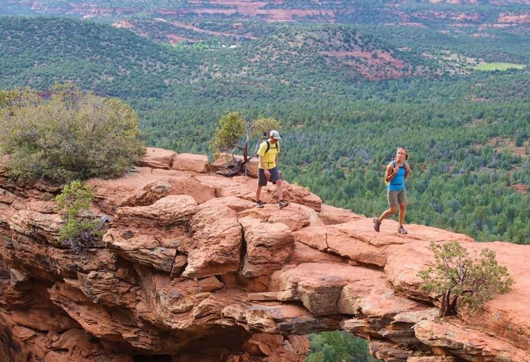 Couple wearing backpacks hiking on a red rock formation during their Margaritaville Vacation Club adventures.