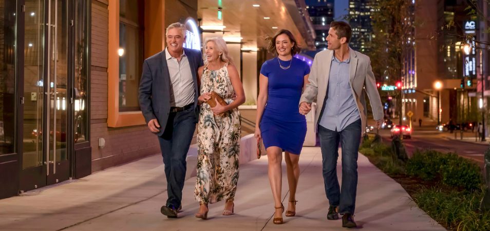 2 couples, holding hands and smiling, walk along the city streets at night during their 3-day trip to Nashville, Tennessee.