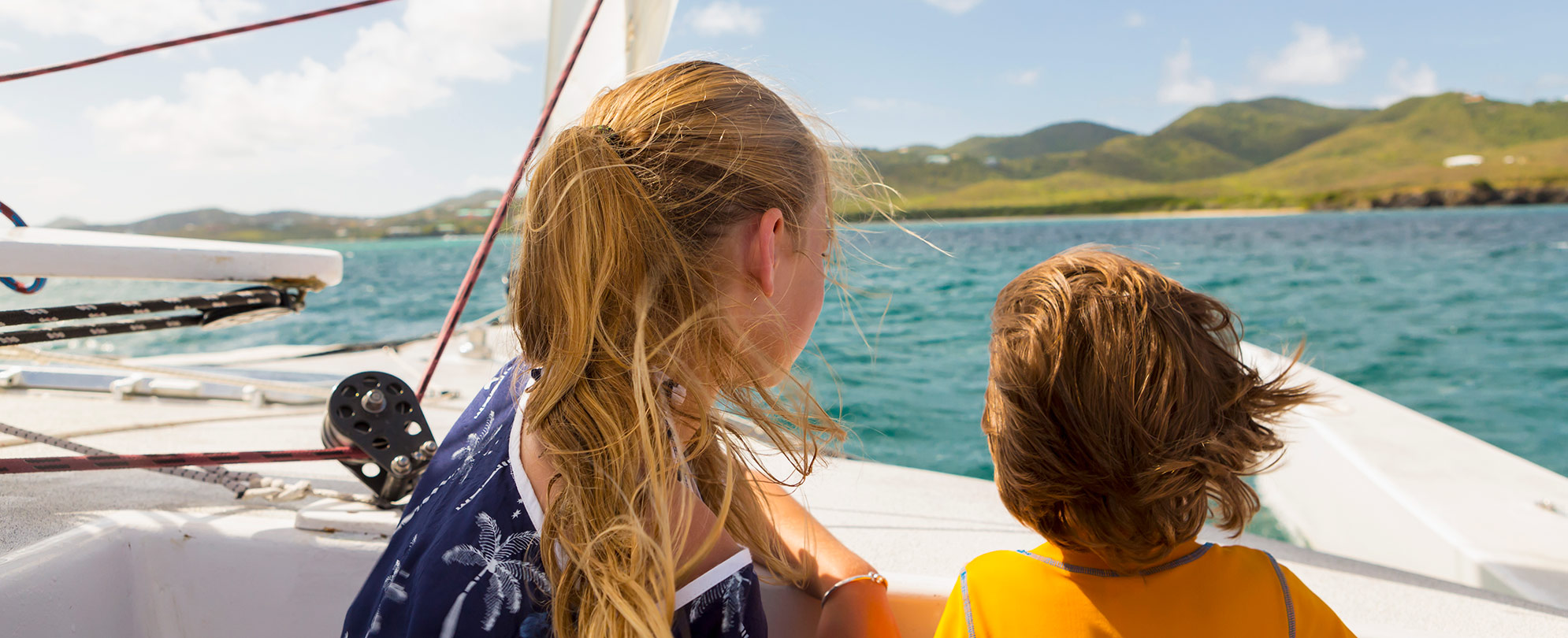 A young boy and girl on a sailboat with small hills in the background in the Virgin Islands National Park.