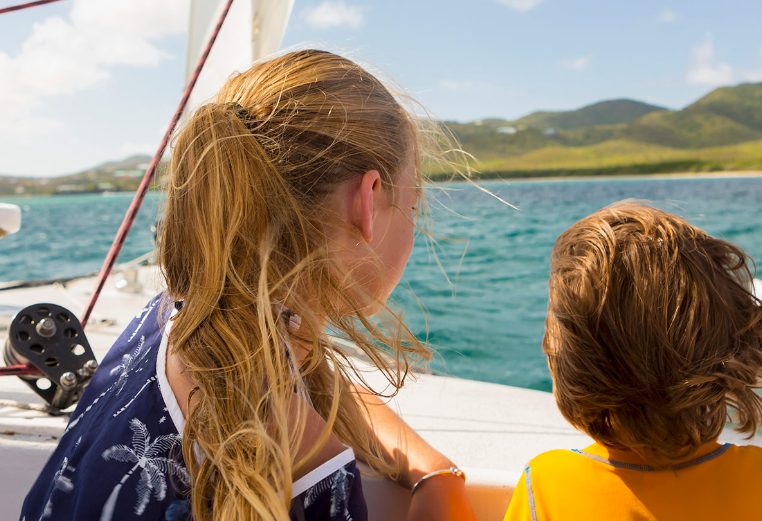 A young boy and girl on a sailboat with small hills in the background in the Virgin Islands National Park.