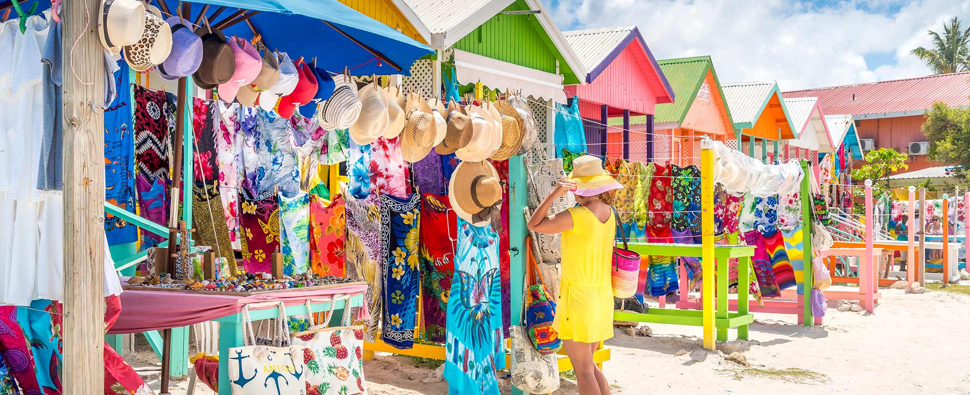 A woman in a yellow dress tries on hats and shops at a colorful outdoor market in Puerto Rico.