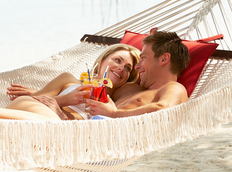 A couple sips rum cocktails together in a hammock on a beach in Puerto Rico