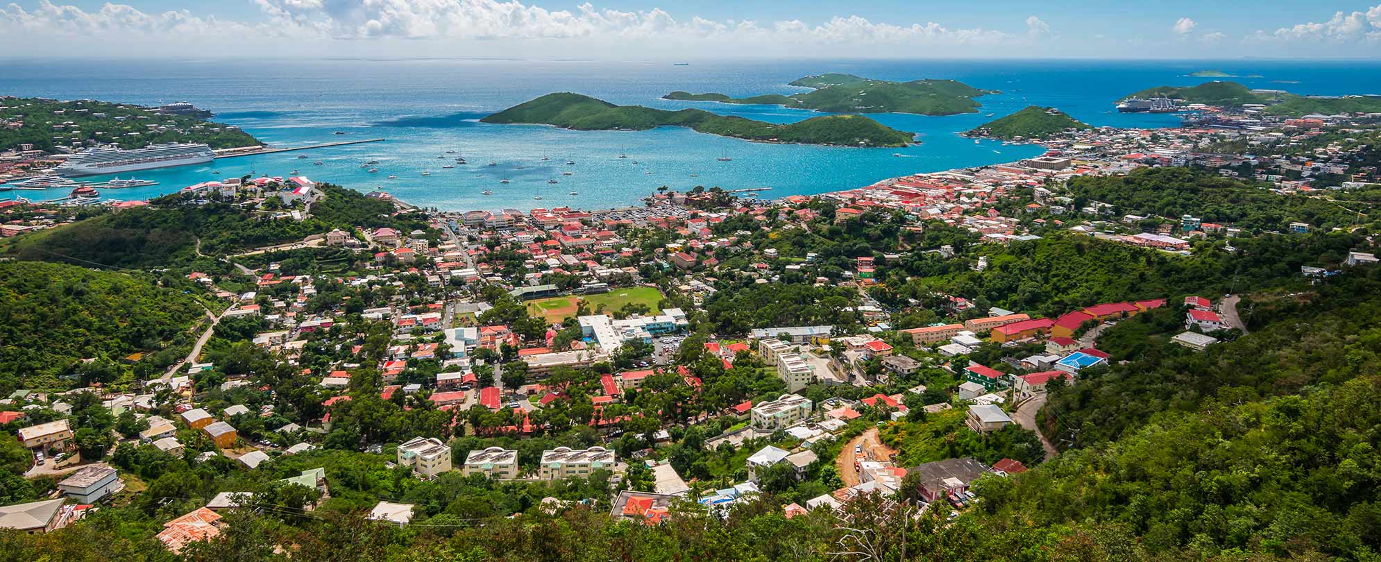A birds-eye-view of St. Thomas, U.S. Virgin Islands, with red-roofed buildings, blue ocean, and lush green landscape.