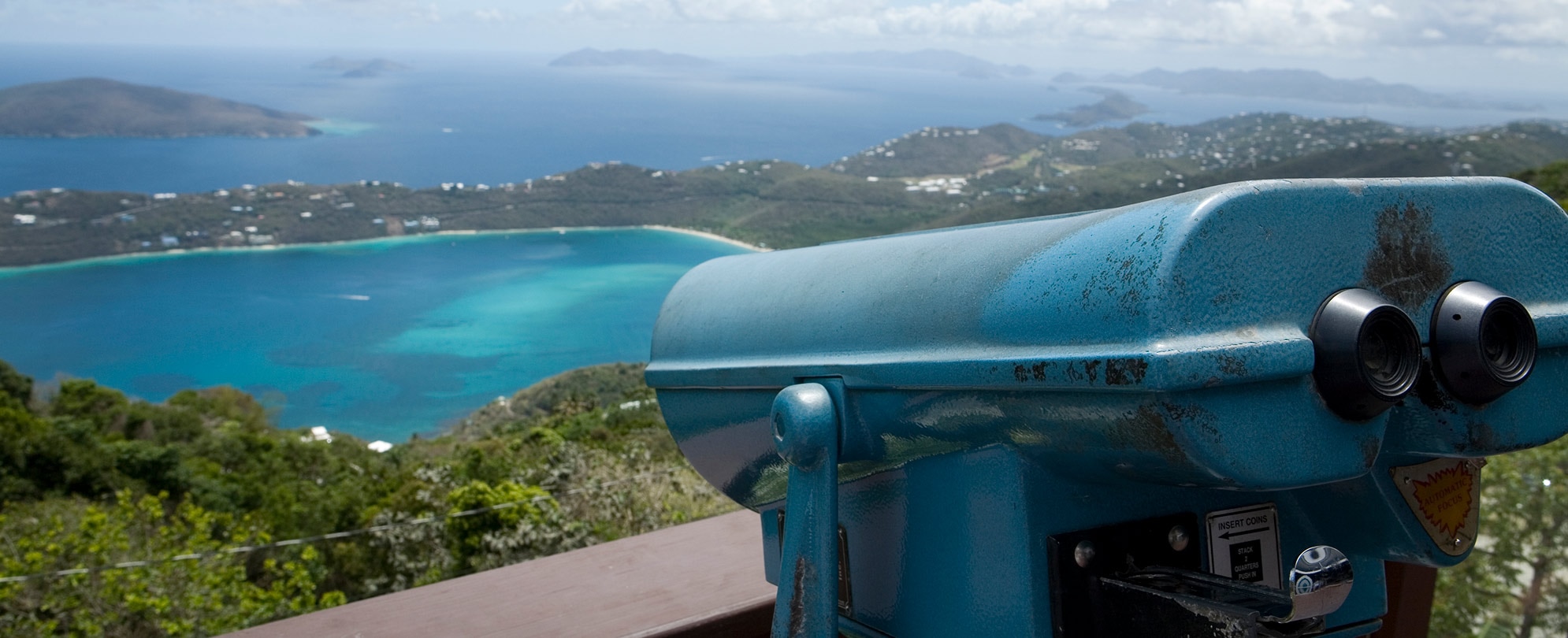 Coin-operated binoculars pointing towards the bright blue waters and lush mountains of St. Thomas, U.S. Virgin Islands.