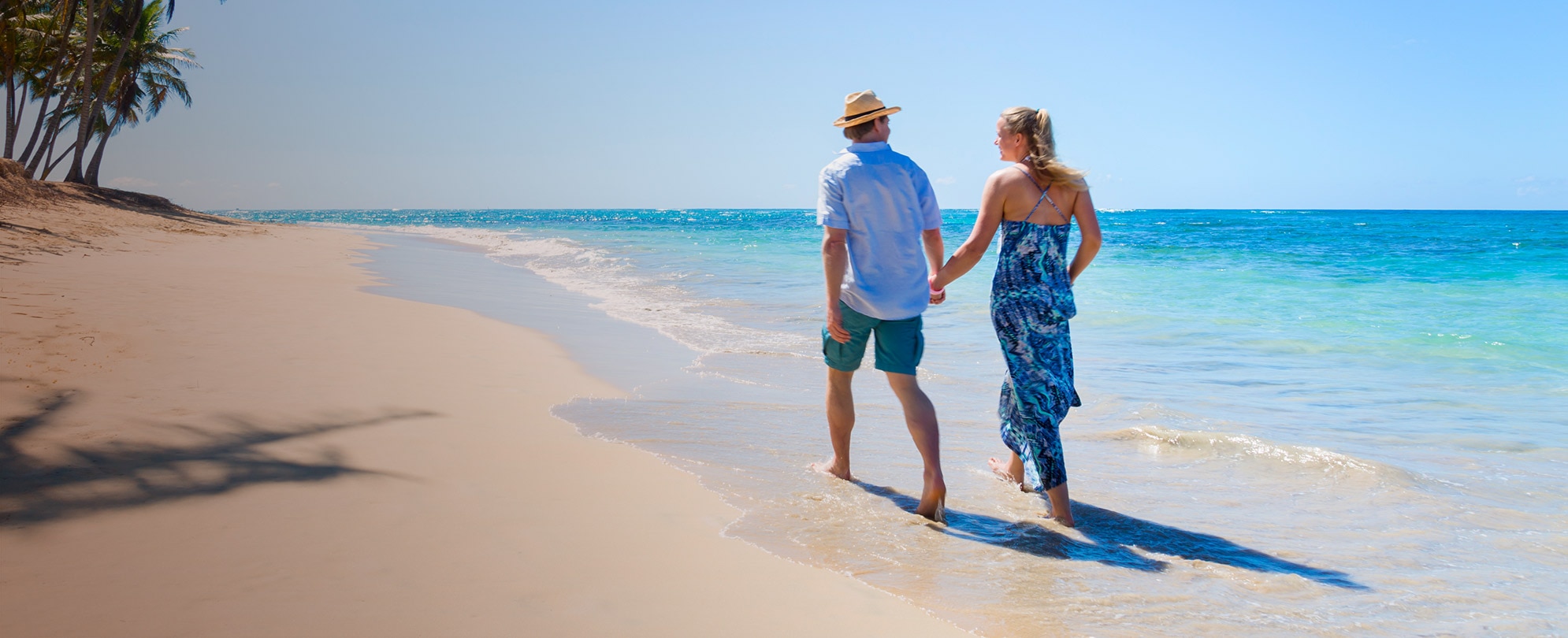 A man and woman holding hands and walking down the beach on their Margaritaville vacation.