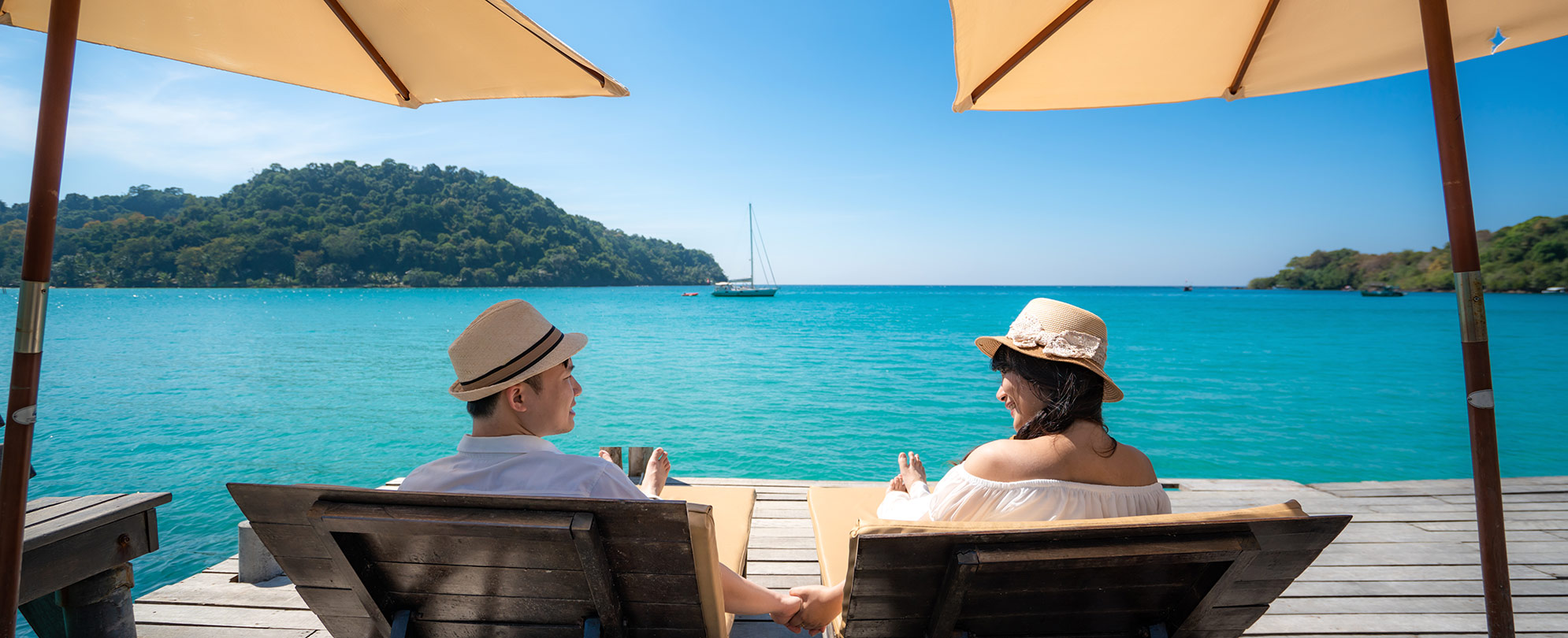 A couple looking at each other while relaxing under umbrellas by the ocean on a tropical vacation.