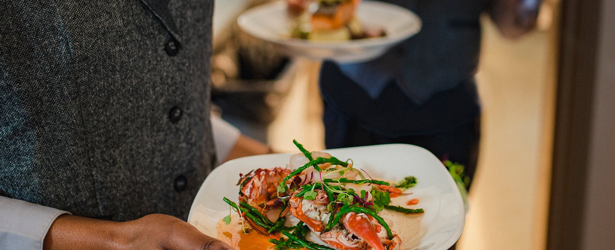 Close-up shot of a waiter holding a plate of seafood and vegetables, about to bring it to a table.