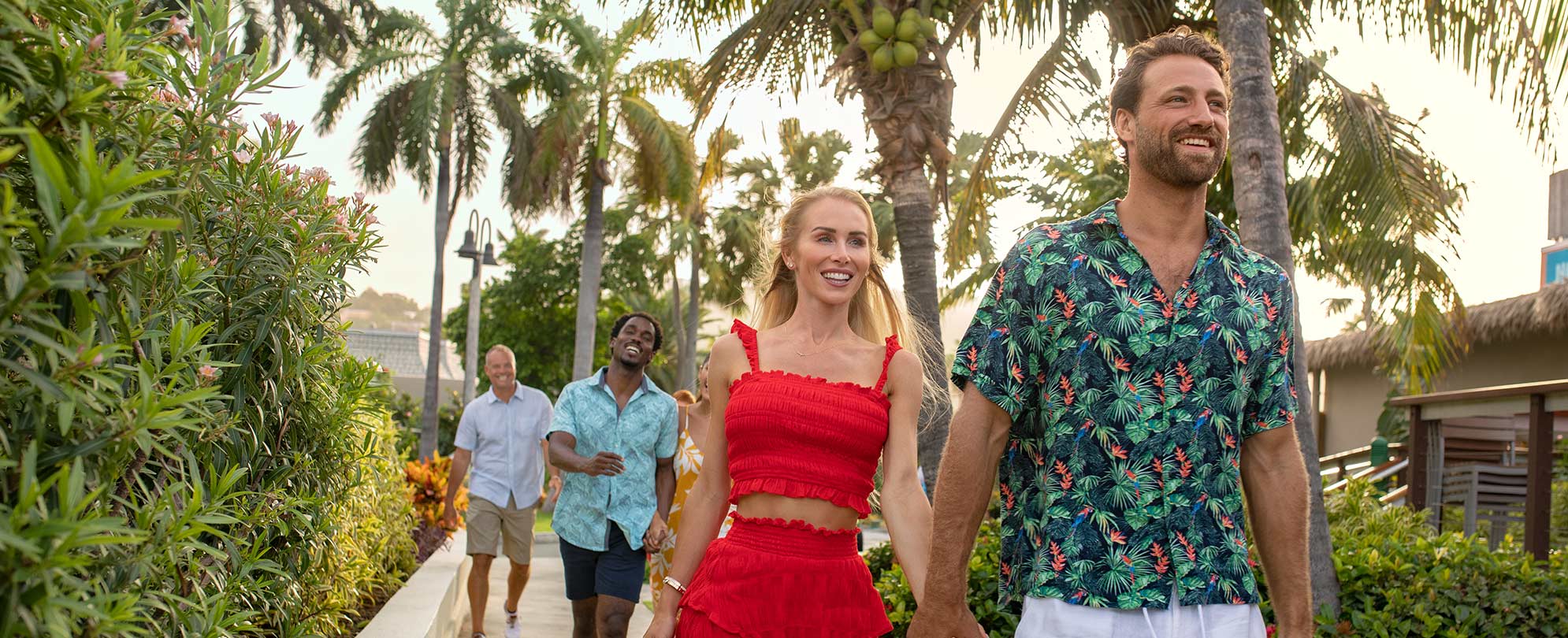Men and women wearing bright, summer clothes, walk along a path surrounded by palms at a Margaritaville Vacation Club resort.
