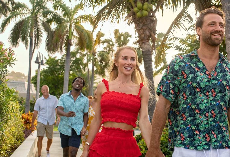 Men and women wearing bright, summer clothes, walk along a path surrounded by palms at a Margaritaville Vacation Club resort.