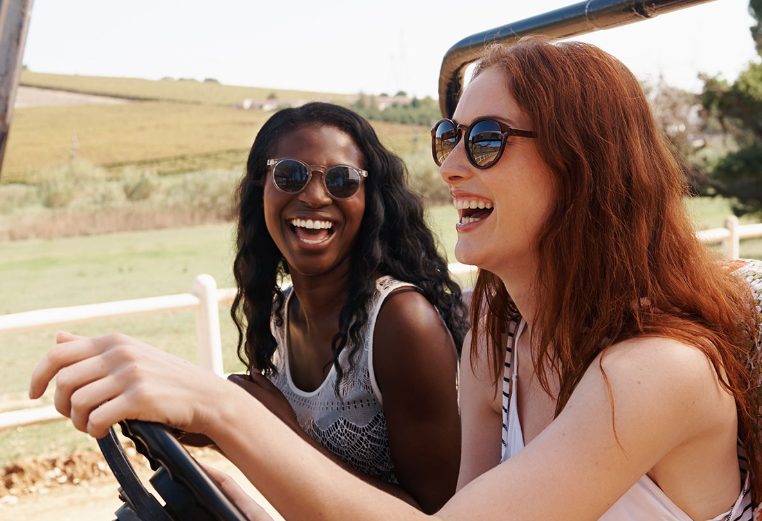 A smiling woman drives a roofless vehicle with her friend in the passenger seat as they enjoy a relaxing, tropical vacation.