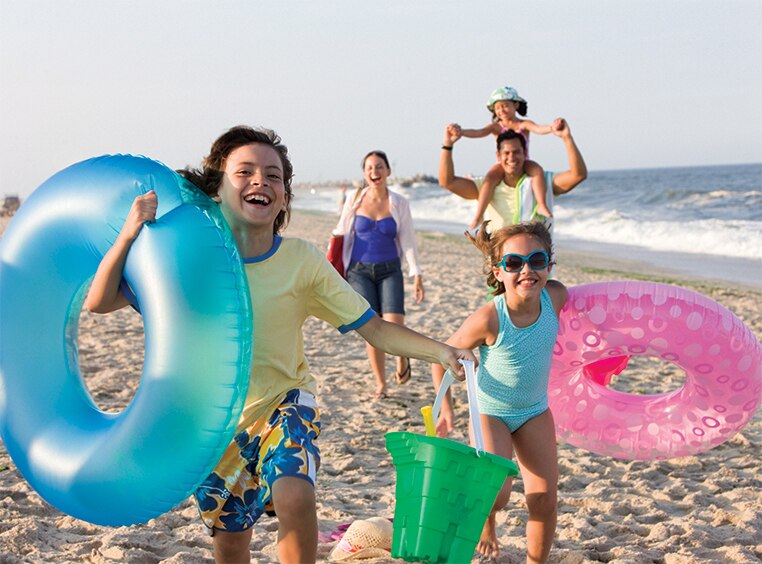 Two kids carrying inflatable tubes walk in front of their mom, dad, and sibling along a national seashore.