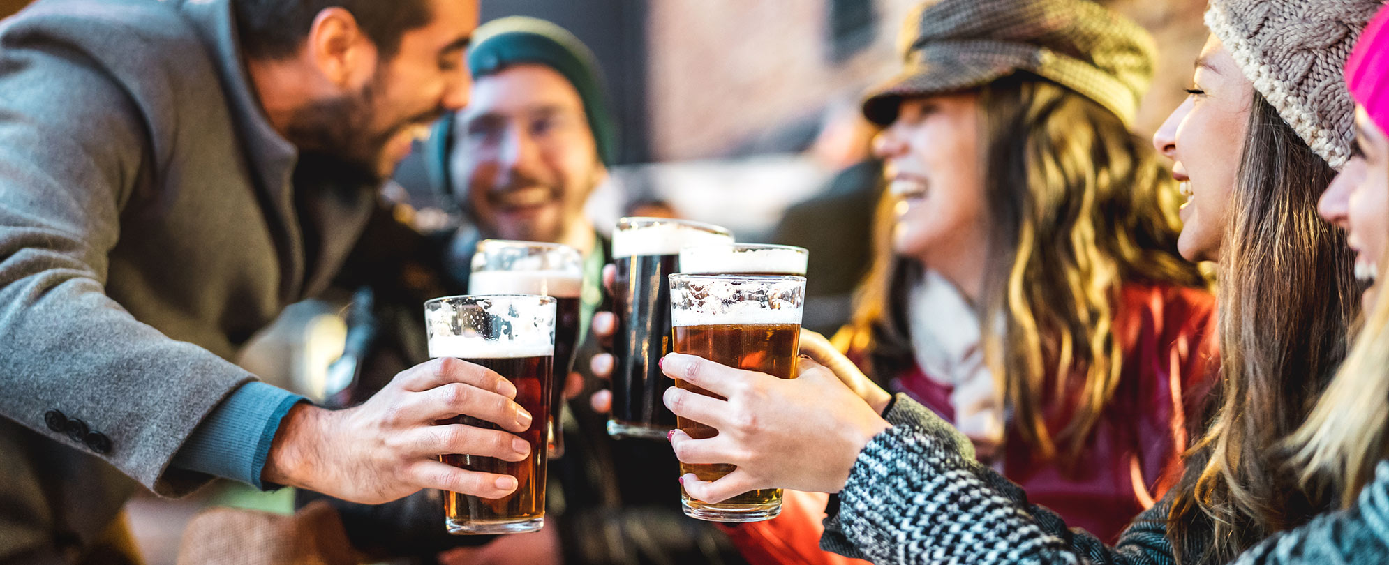 A group of friends wearing cold weather clothes share a toast by clinking their pints of beer.