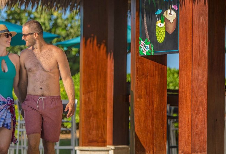 A husband and wife walk together in their bathing suits past the poolside bar at the Margaritaville Vacation Club by Wyndham - Rio Mar resort in Puerto Rico