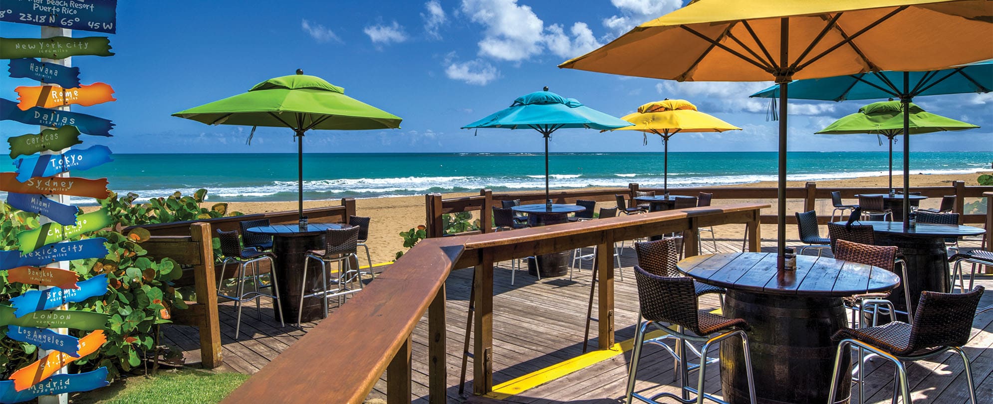 Wood tables with colorful umbrellas on a beachfront deck at Margaritaville Vacation Club by Wyndham - Rio Mar.