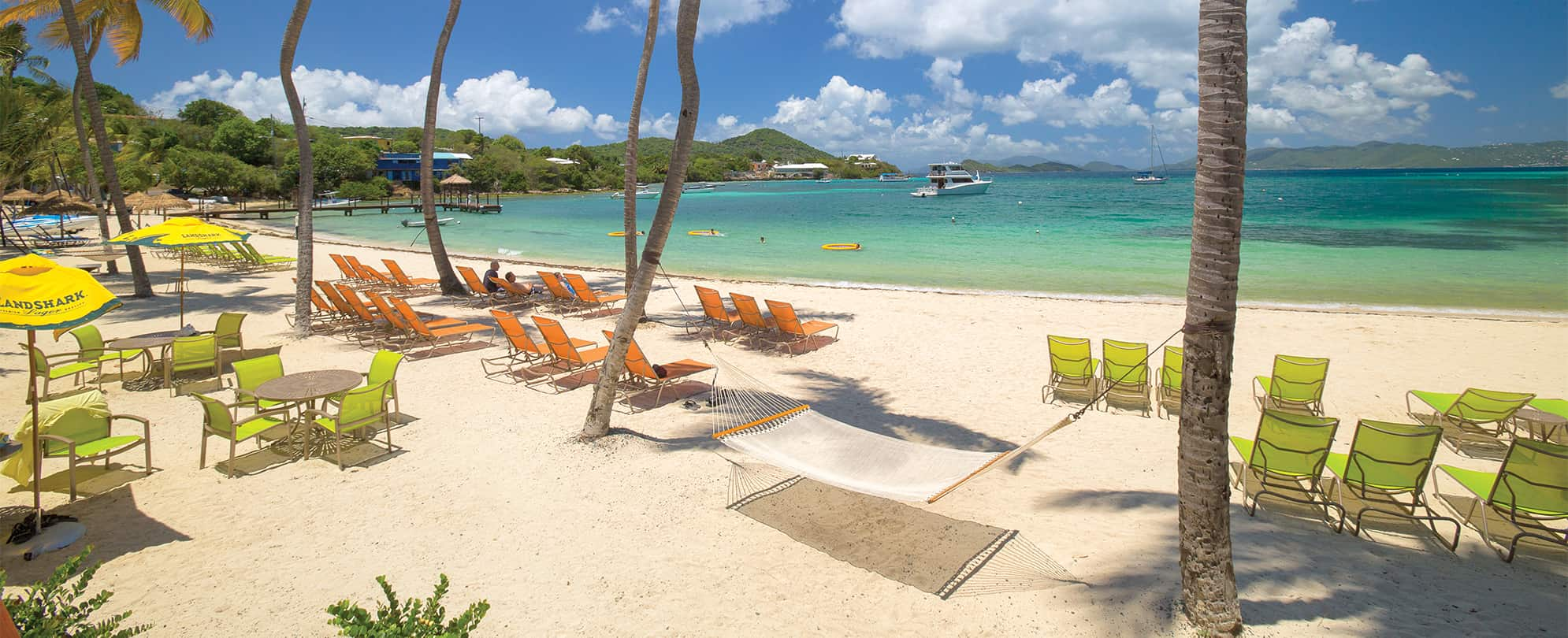 A hammock and chairs under palm trees by the ocean at Margaritaville Vacation Club by Wyndham - St. Thomas.