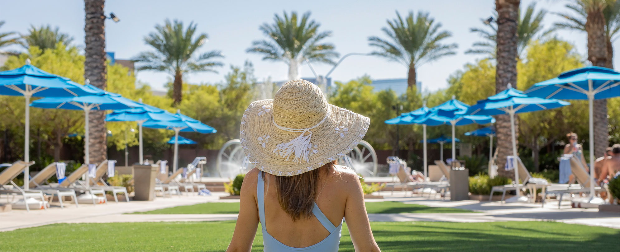 A woman wearing a straw hat looking at palm trees at Margaritaville Vacation Club by Wyndham - Desert Blue in Las Vegas, NV.